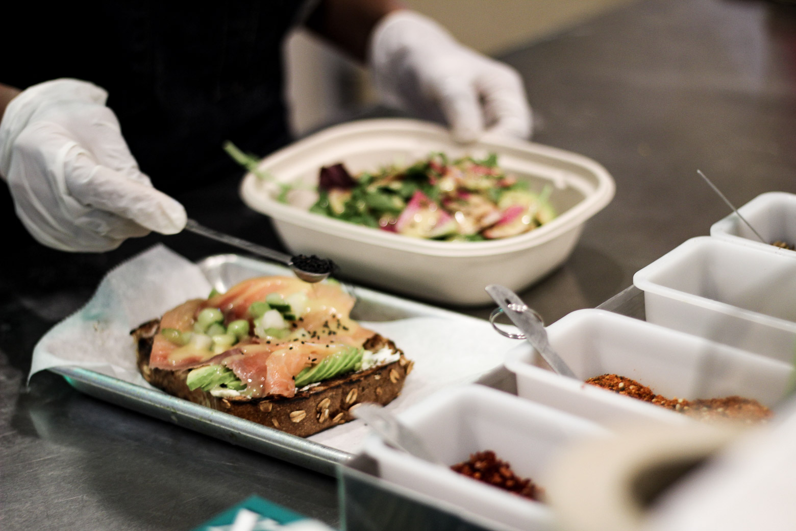 Staff member garnishing avocado toast with lox