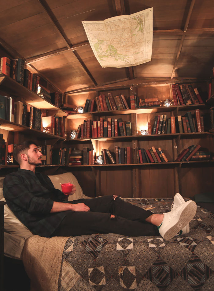 Man sitting on a bed in a lodge surrounded by books and a map in a bar